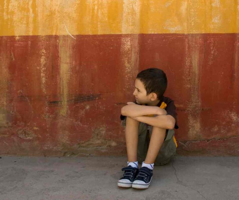 A boy sitting alone on the floor looking right.