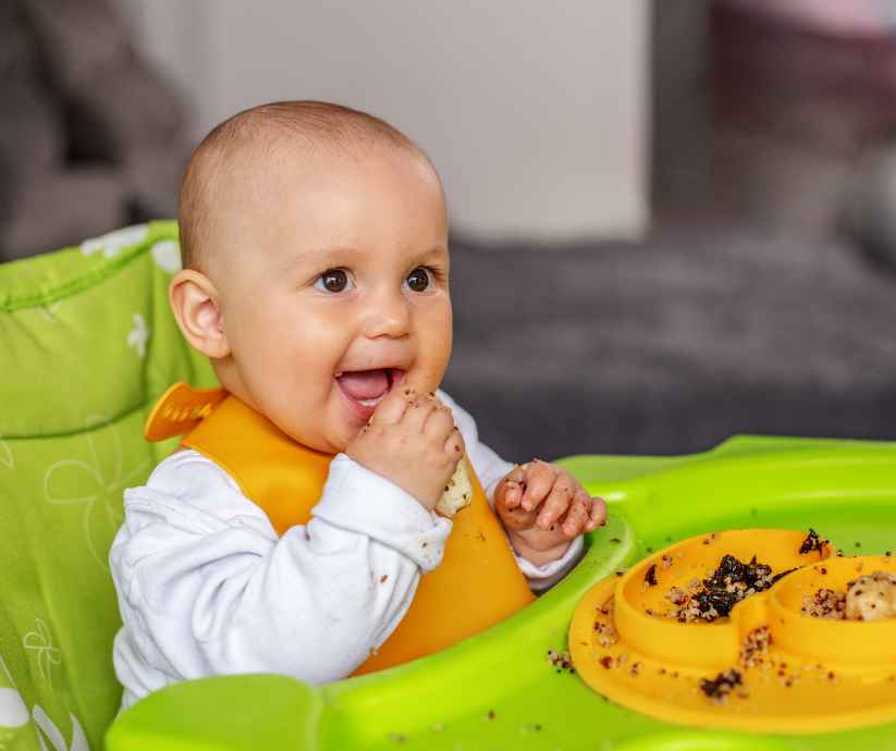 Baby is eating food with his hands.